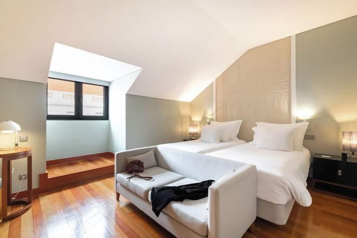 Un dormitorio con cama, sofá, mesita de noche, lámpara y ventana.
