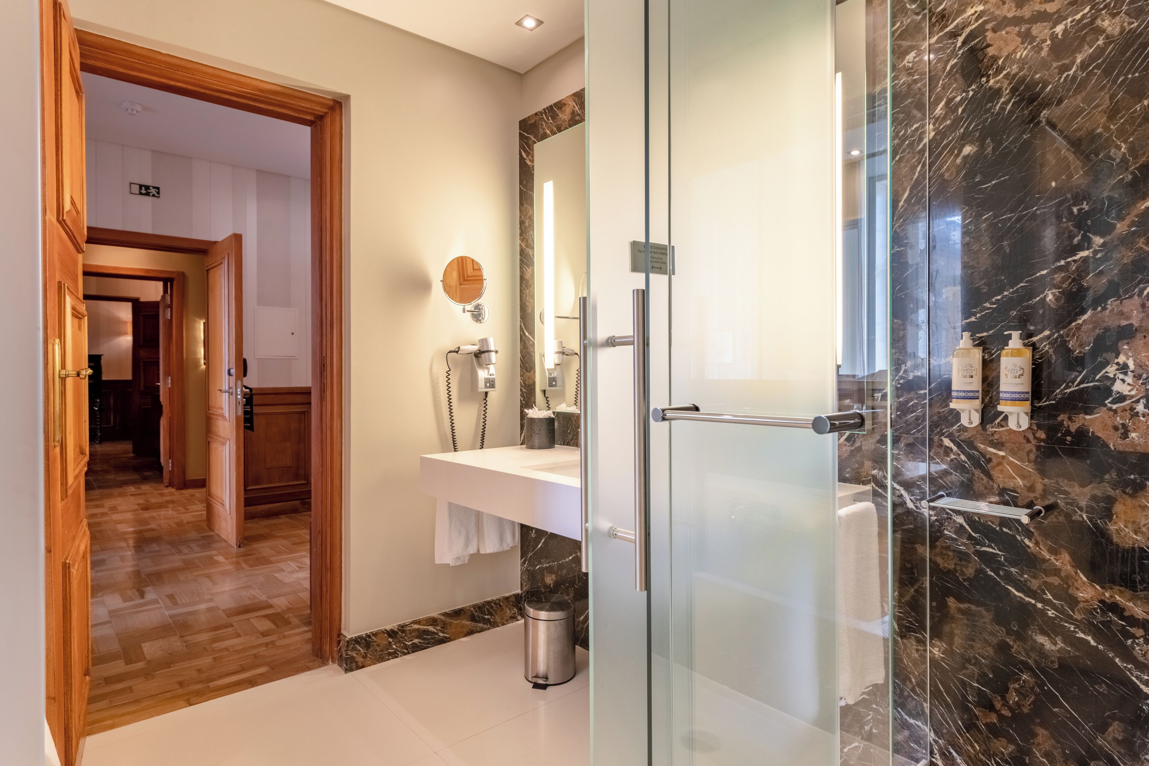 A modern bathroom with a glass shower enclosure, a marble backsplash, and a white sink with a mirror.