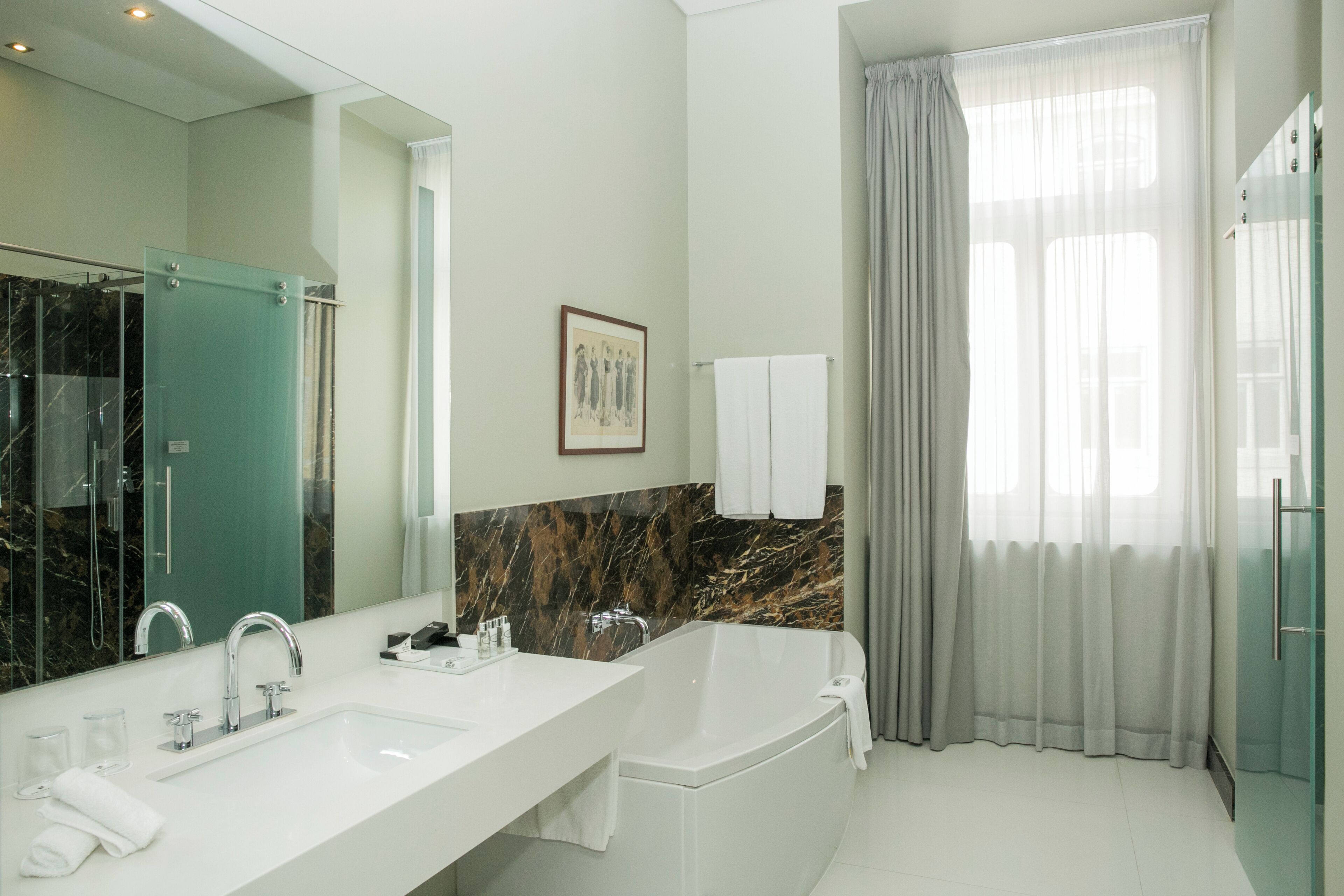 Un baño moderno con un espejo grande, un salpicadero de mármol, un lavabo doble y una bañera.