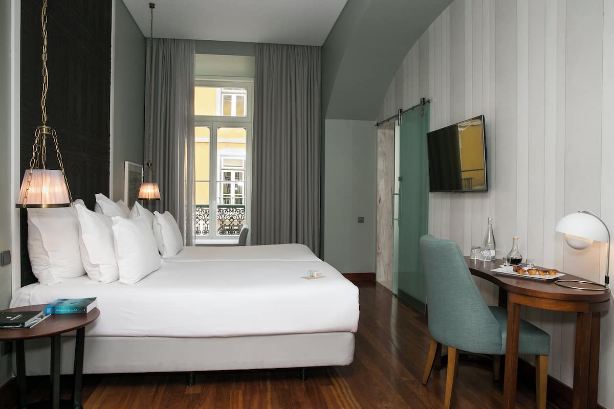 Habitación de hotel con una cama grande, un escritorio con silla, un televisor y una ventana con cortinas.