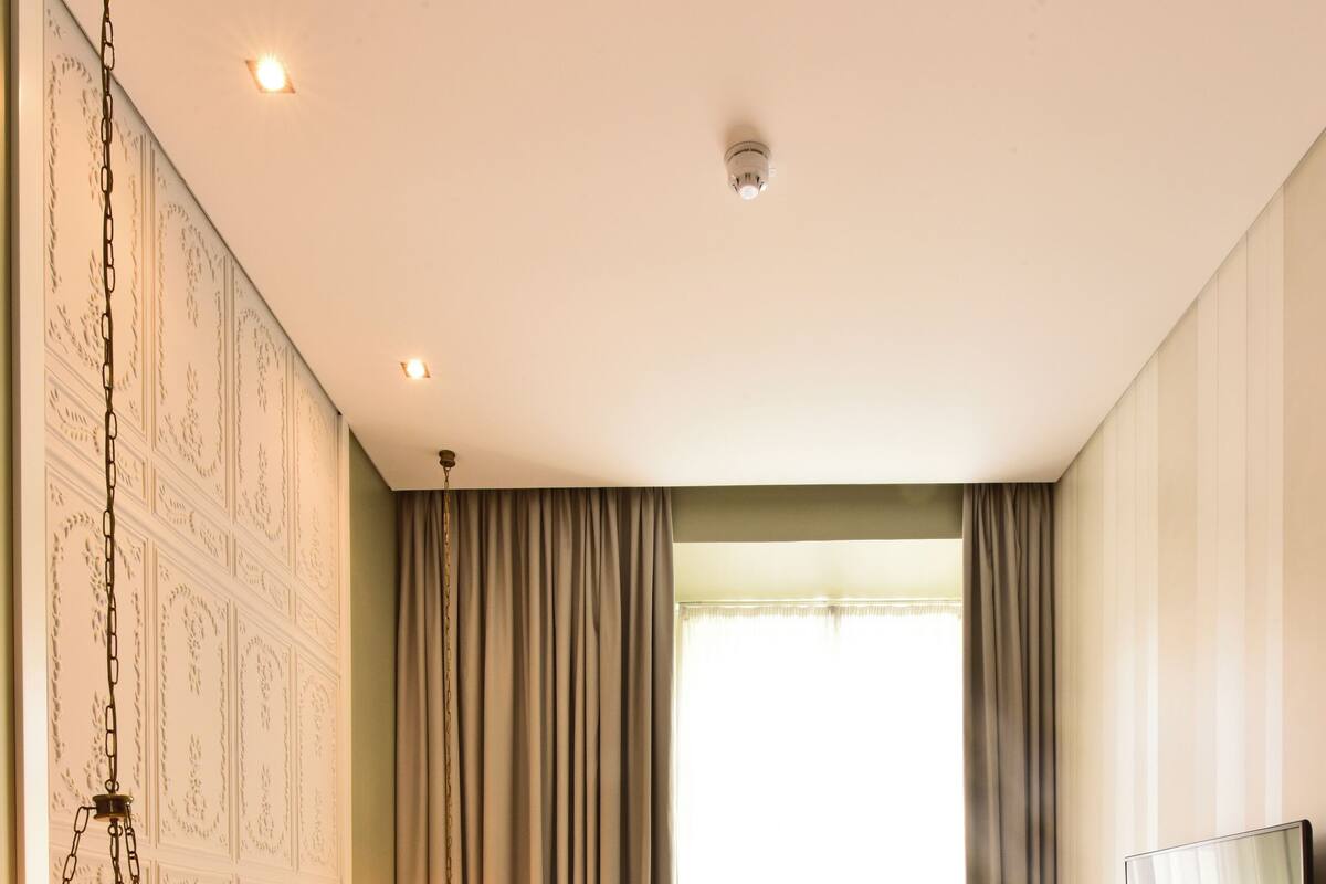 Habitación de hotel con cama, escritorio, silla, televisor y ventana con cortinas.