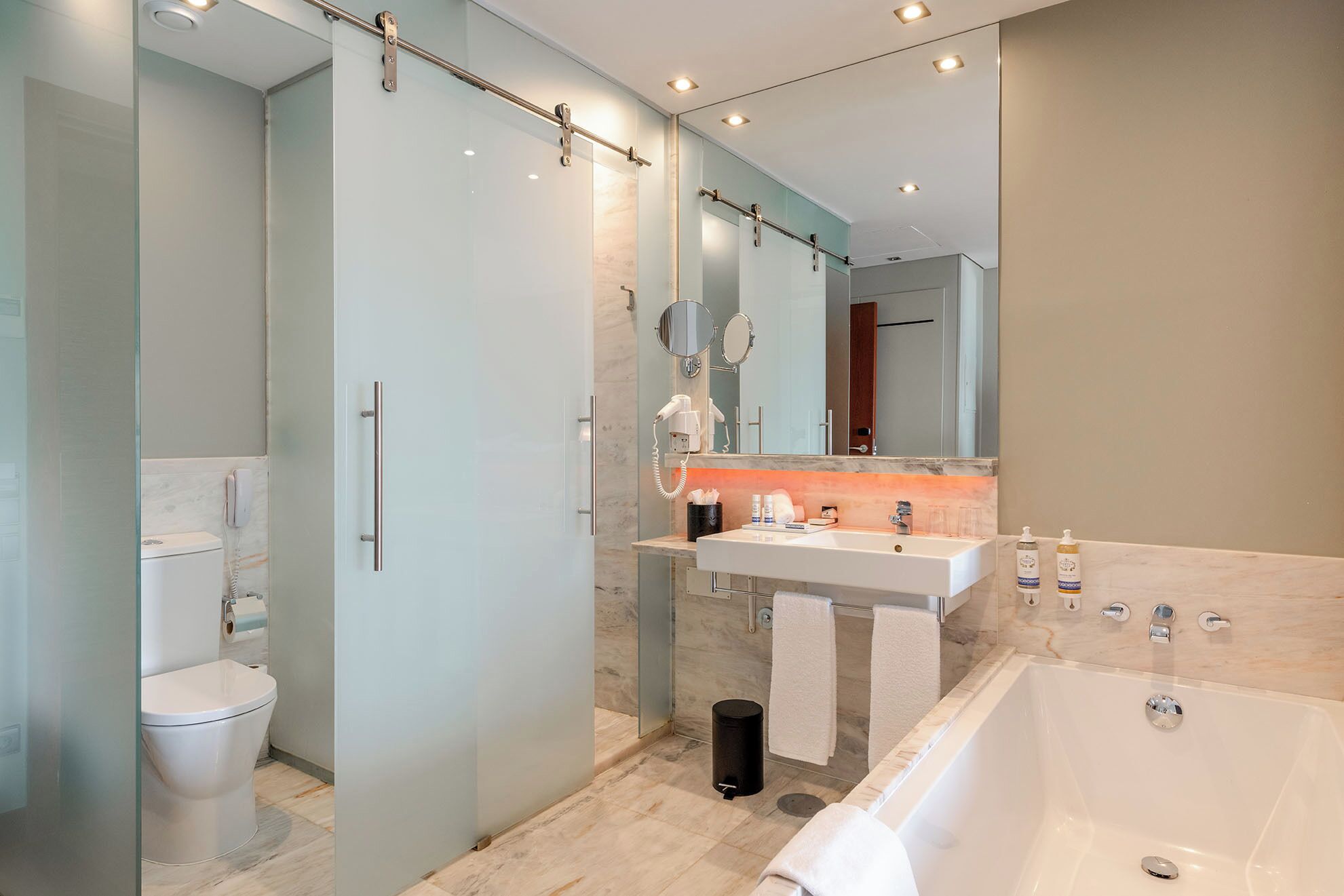 A modern bathroom with a glass shower enclosure, a white toilet, a sink with a vanity, a large mirror, and a bathtub.
