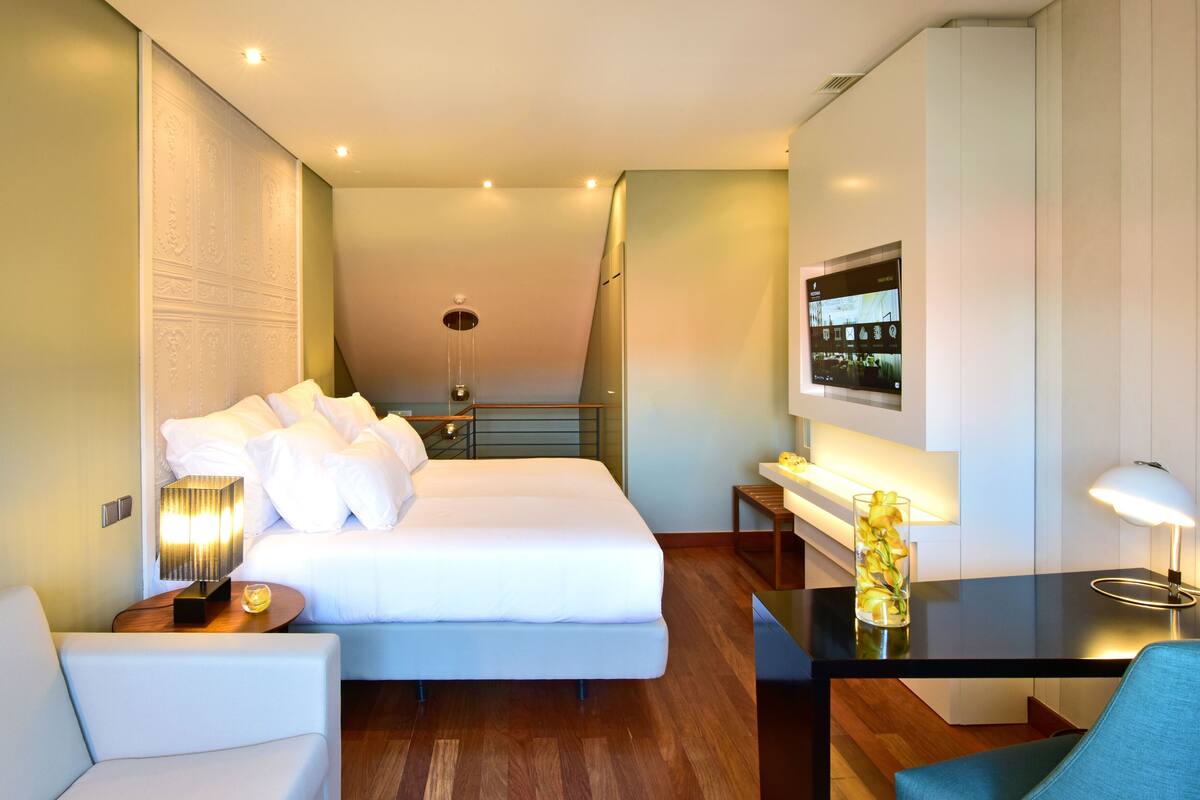 Una habitación de hotel moderna con una cama grande, un escritorio, una silla y un televisor montado en la pared.
