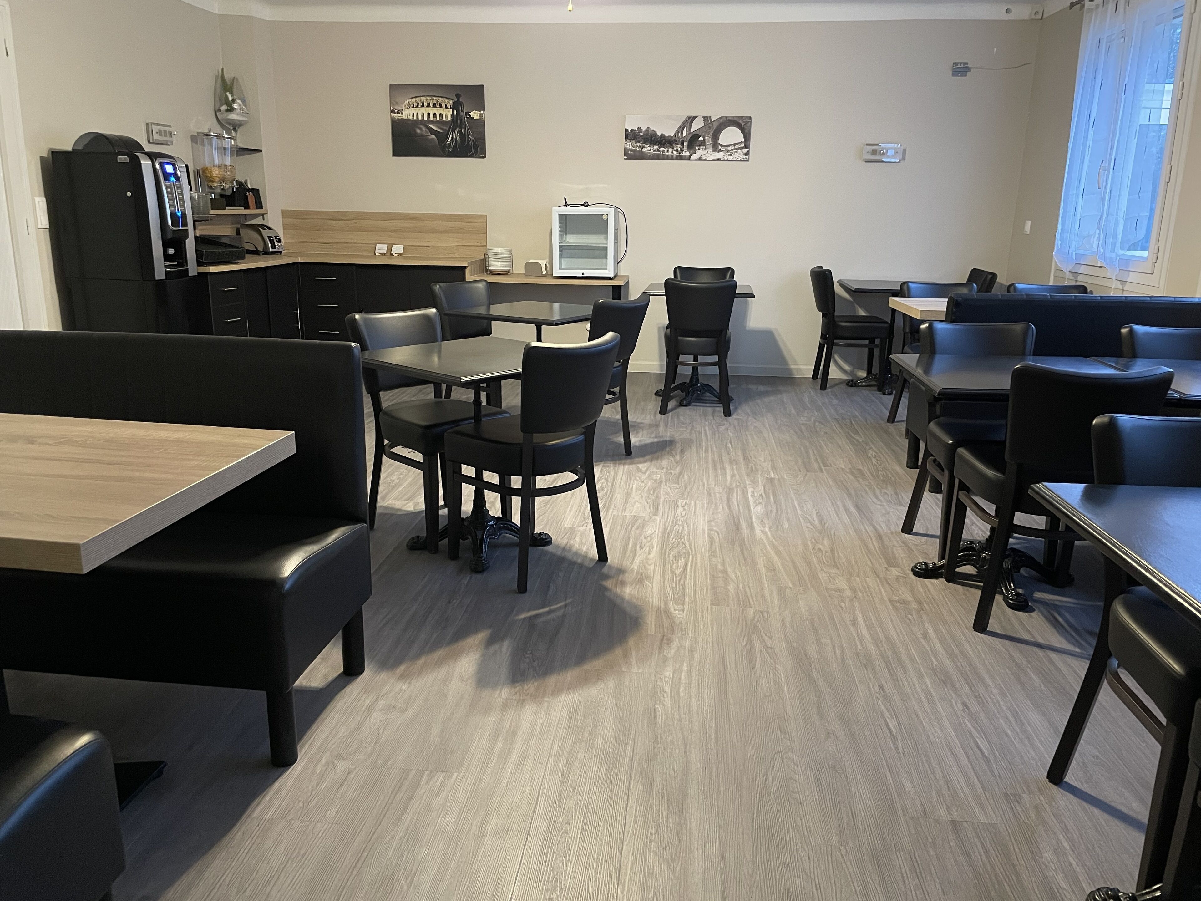 A modern dining area with black chairs and tables, a coffee machine, and a TV screen.