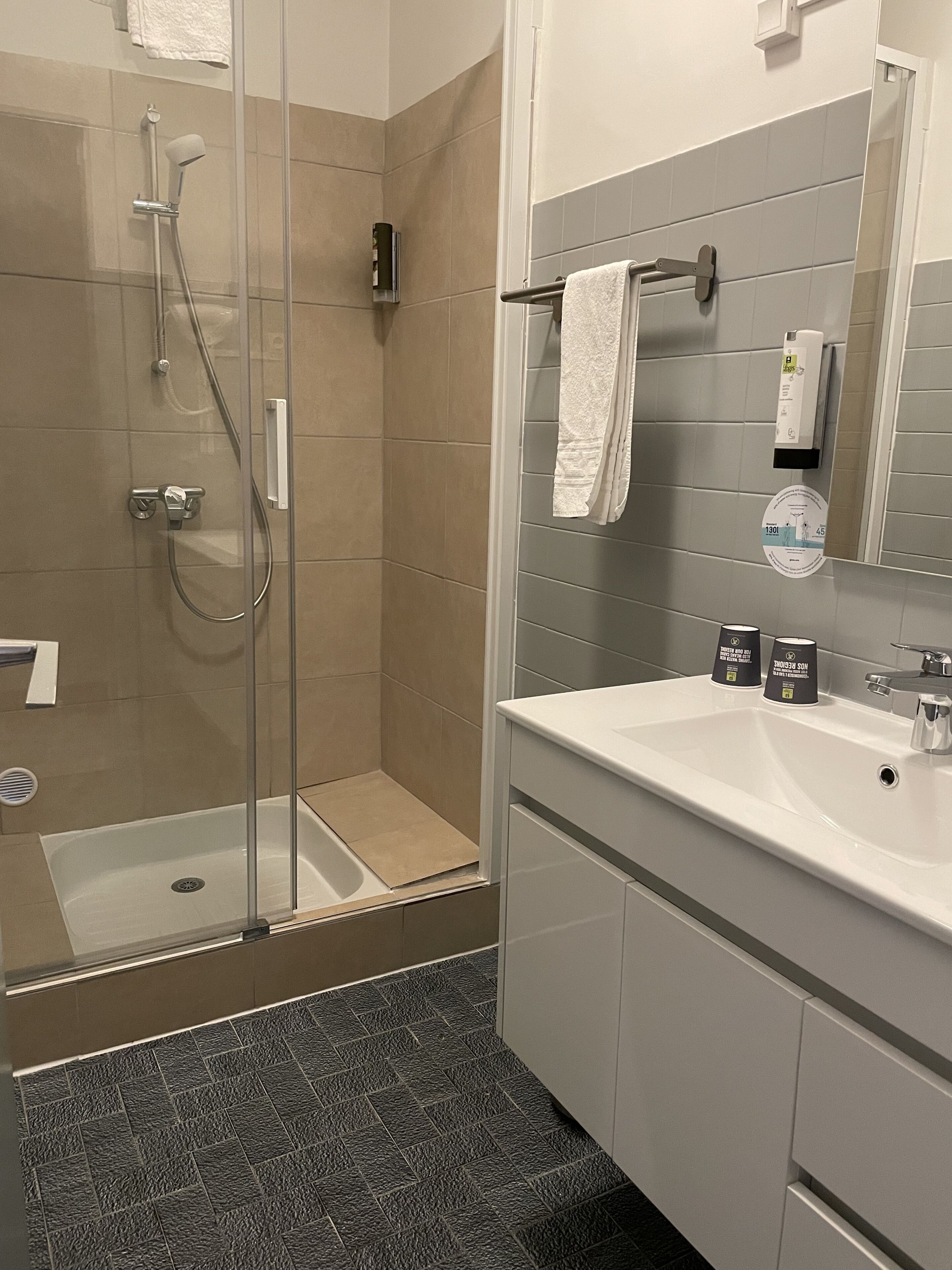 A modern bathroom with a glass-enclosed shower, a white sink, and a mirror with a towel rack.
