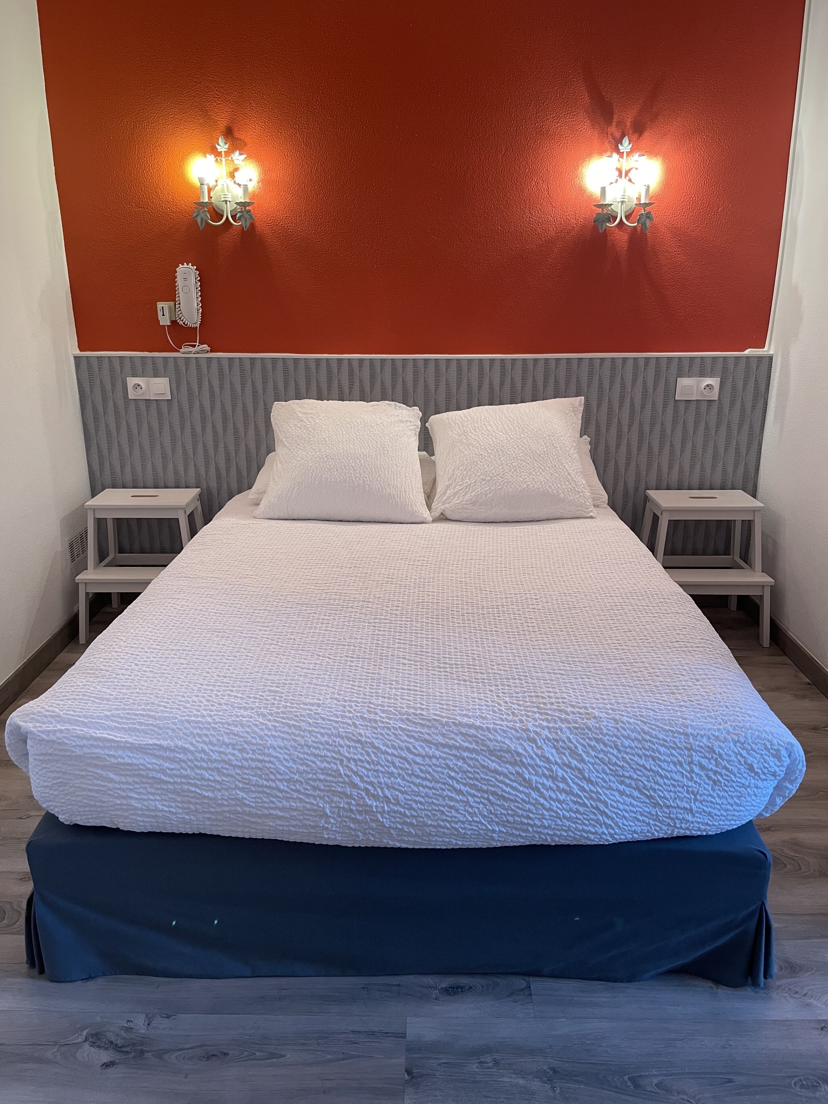 Une chambre d’hôtel avec un grand lit, deux tables de chevet, un téléphone fixé au mur et deux appliques murales.