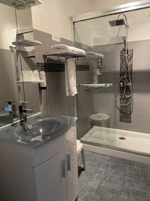 Un bany modern amb dutxa envidriada, un lavabo de vidre i un moble de bany amb paraireula.