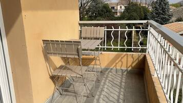 A balcony with a metal table and chairs, a white railing, and a view of a residential area.