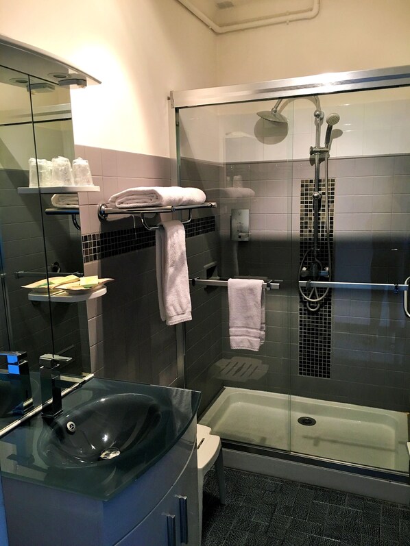 Un baño moderno con cabina de ducha de vidrio, lavamanos negro y puerta de ducha de cristal.