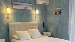 A bedroom with a white bed, two bedside tables, a wall-mounted phone, and an air conditioning unit. - Hotel Le Clément V (Roquemaure)