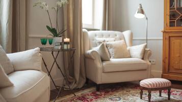 Een woonkamer met een beige bank, een bijpassende fauteuil, een klein voetenbankje, een vloerlamp en een vloerkleed met een patroon.