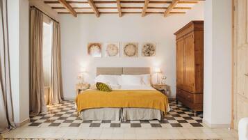 Un dormitorio con piso a cuadros, cama con manta color mostaza, cabecera de madera, lámparas de noche y un armario de madera.