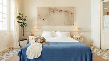 A bedroom with a large bed, two bedside tables, a potted plant, and a painting on the wall.