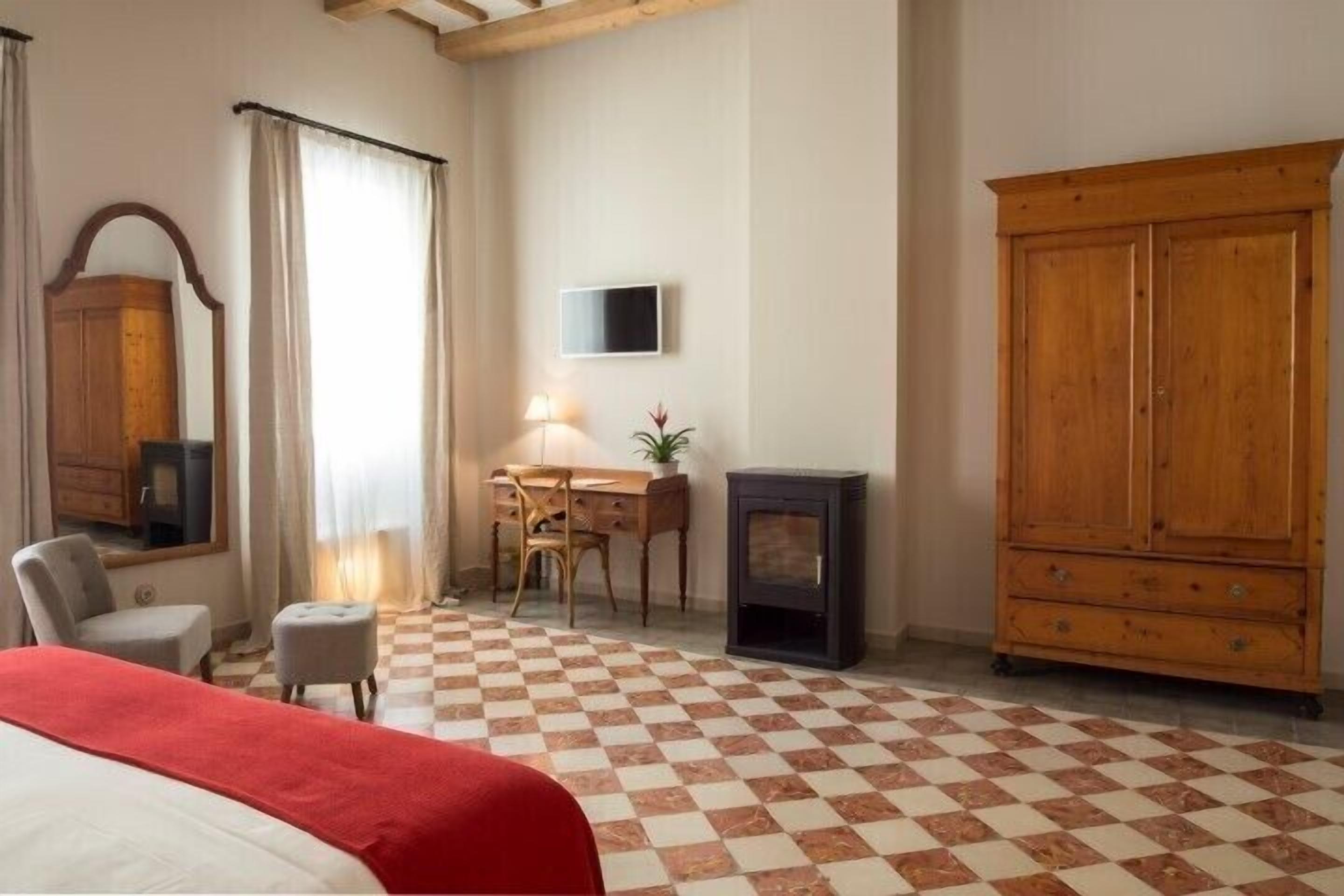 Habitación de hotel con una cama, un escritorio con lámpara, televisión, armario y chimenea.