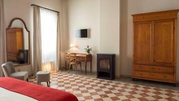 Habitación de hotel con una cama, un escritorio con lámpara, televisión, armario y chimenea.