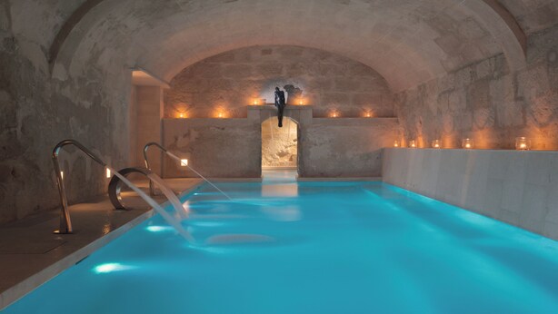 An indoor swimming pool with arched stone ceilings and a central statue. - Jardí de ses Bruixes Boutique Hotel (Mahón)