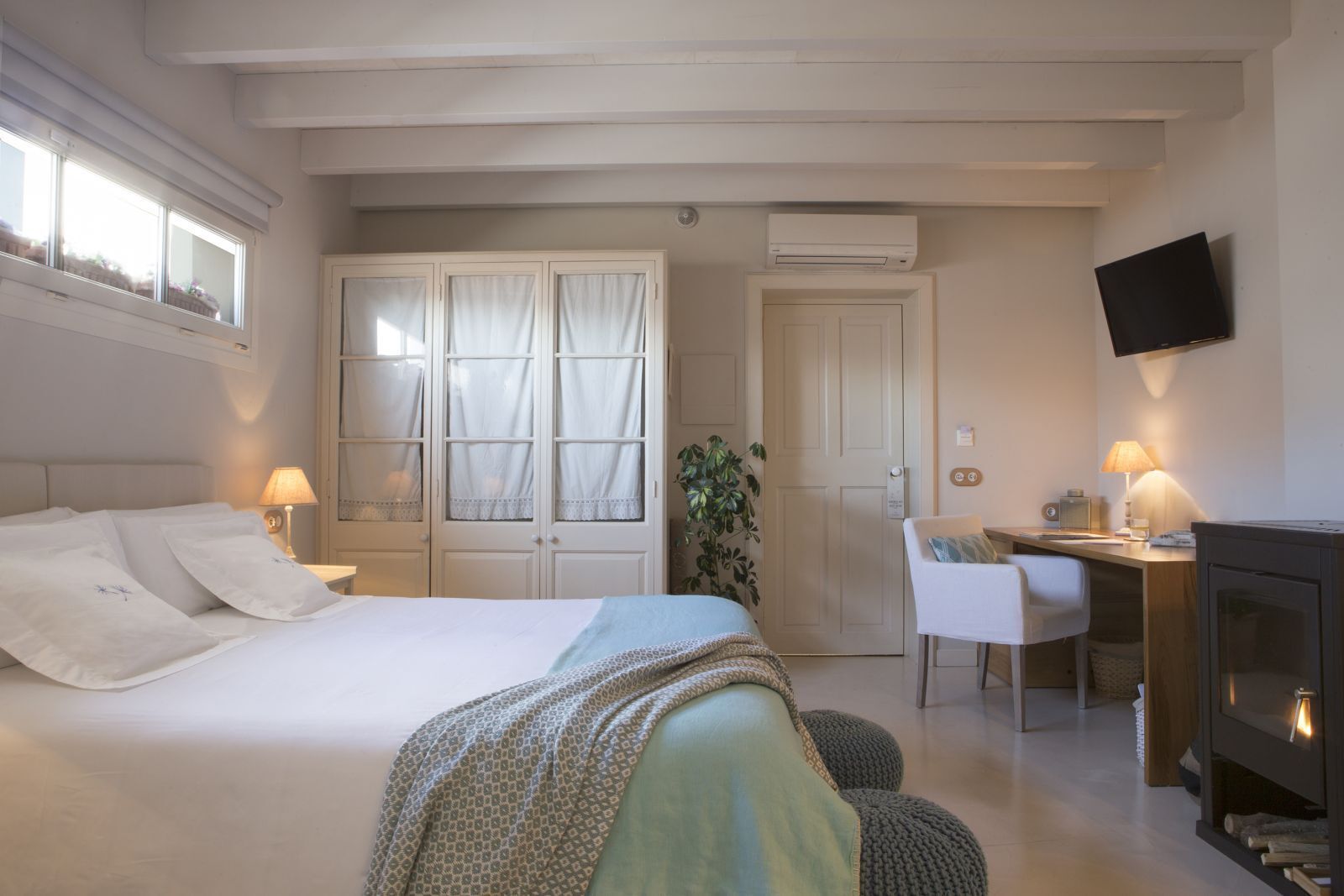 A hotel room with a bed, a desk, a chair, a television, and an air conditioning unit.