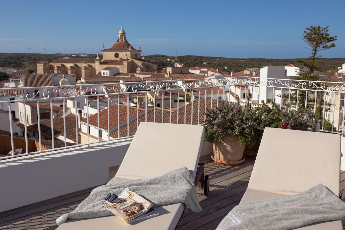 A balcony with two lounge chairs, a potted plant, and a view of a historic building in the background.