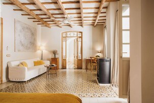 Una habitación con un sofá blanco, una mesita, una lámpara, un cubo de basura y un suelo estampado.
