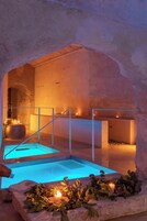 Un área de piscina interior con un arco de piedra, un banco de madera y velas.
