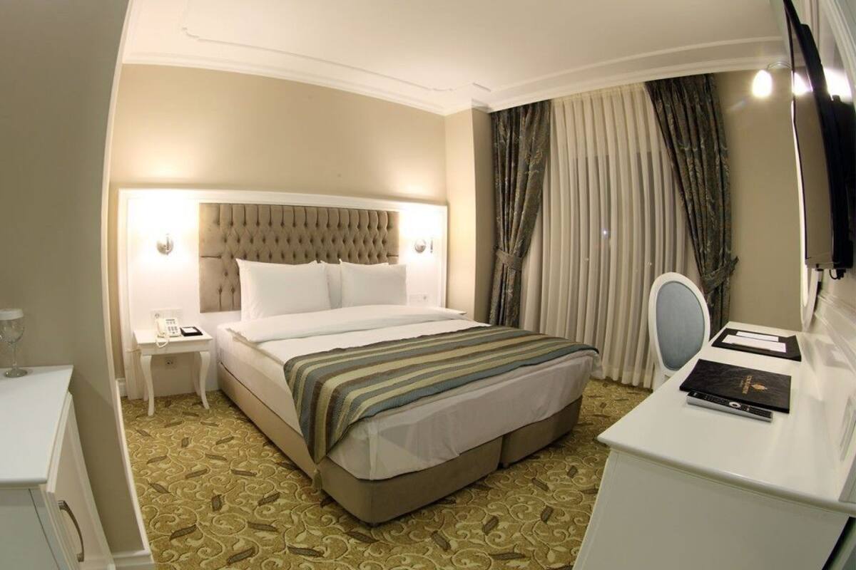 A hotel room with a bed, bedside table, lamp, and a desk with a chair.