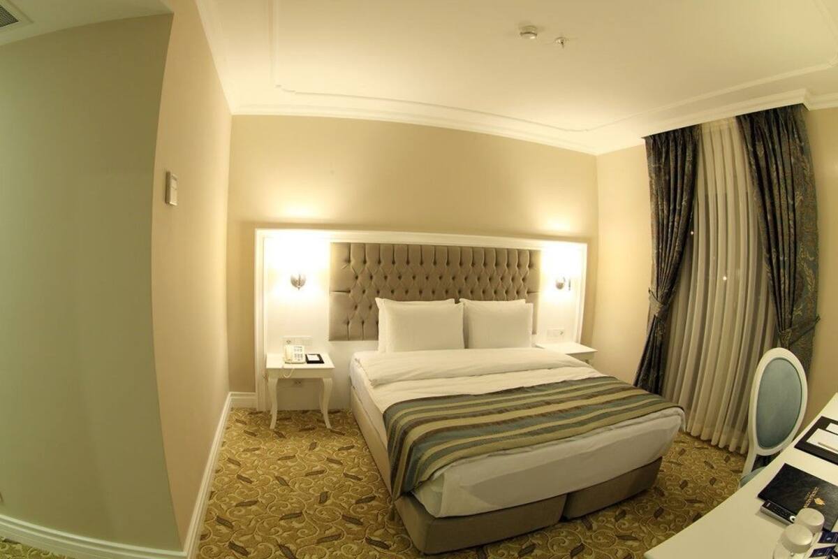A hotel room with a large bed, a bedside table with a lamp, a small table with a phone, and a mirror.