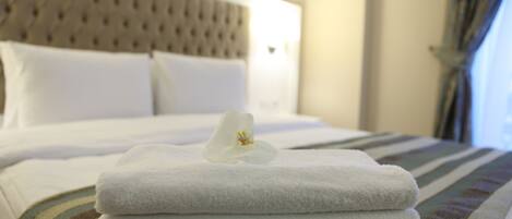 A neatly made bed with white towels and a single flower on top, a tufted headboard, and a striped pillowcase.