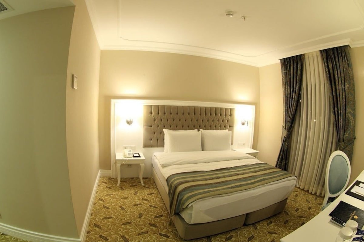 Una habitación de hotel con una cama grande, una mesita de noche con una lámpara, una pequeña mesa con un teléfono y un espejo.