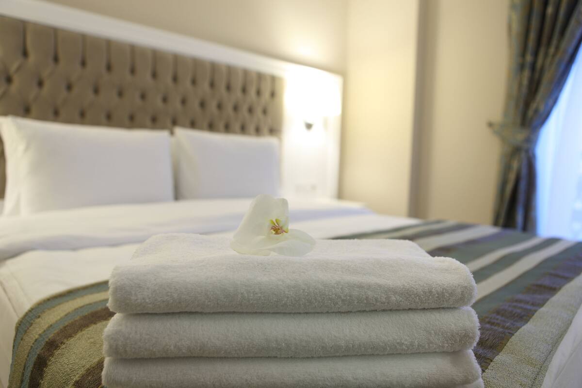 A neatly made bed with folded white towels and a single white flower.