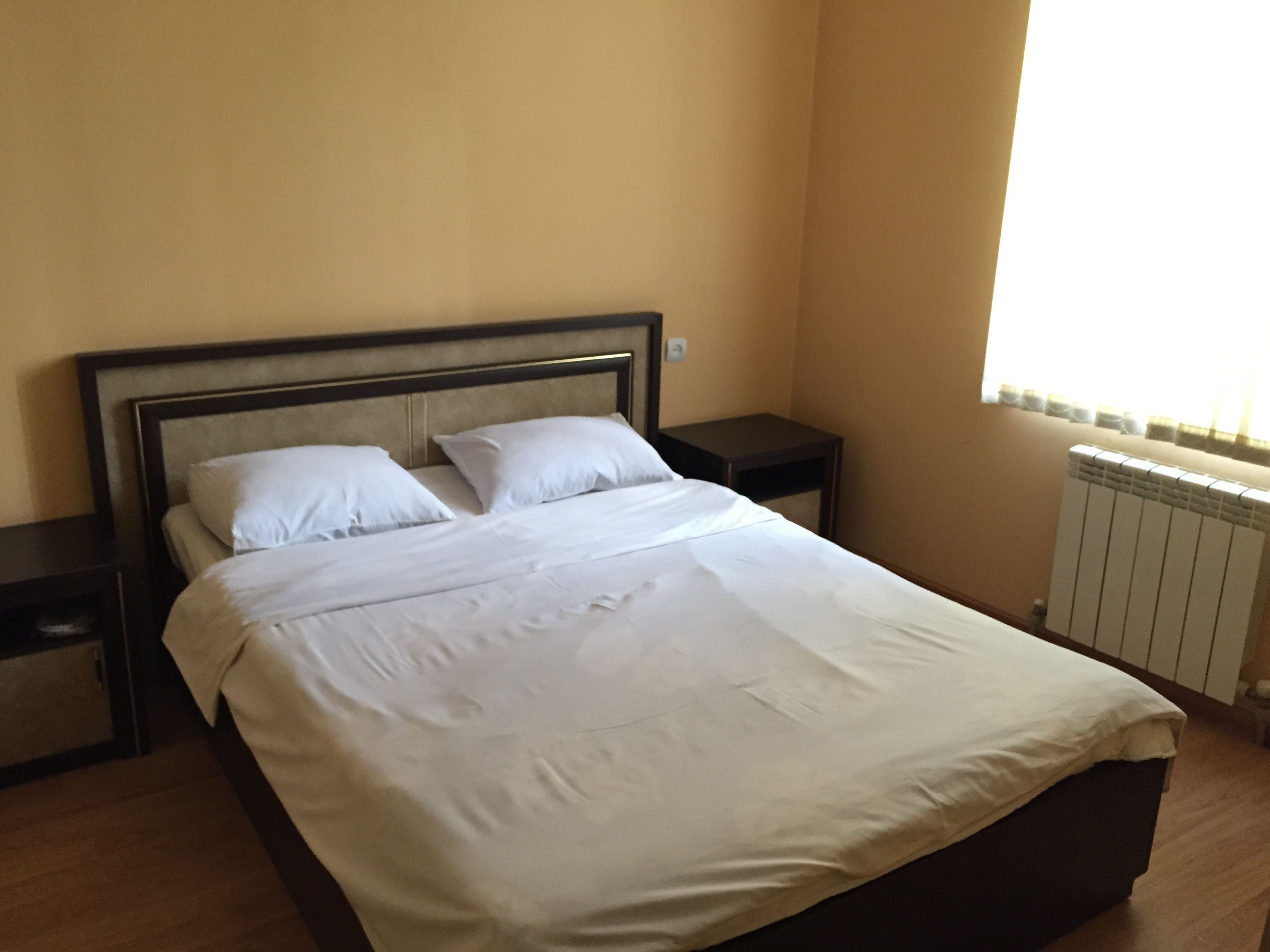 A neatly made bed in a room with a wooden headboard, a nightstand, and a radiator.