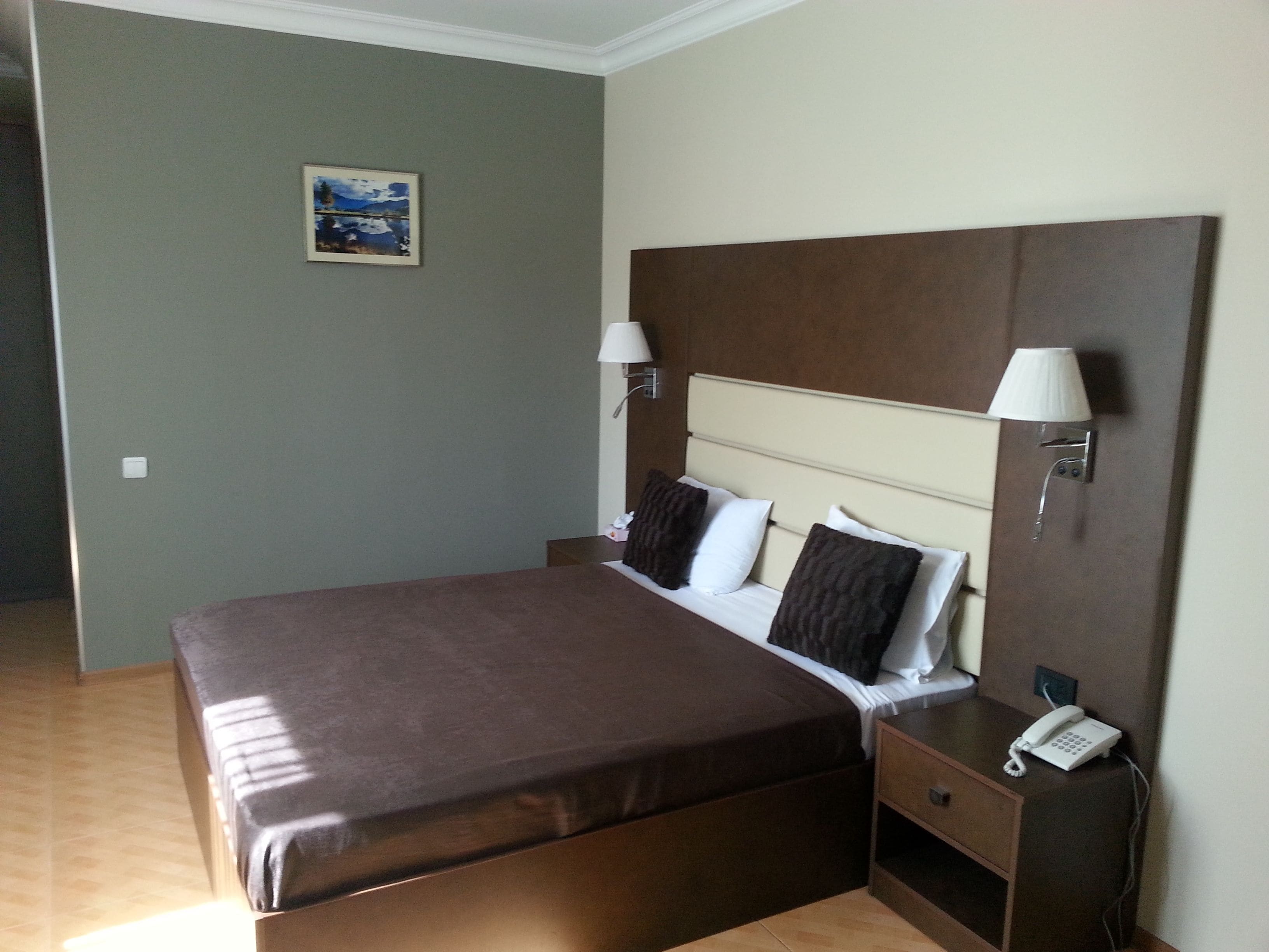A neatly arranged hotel room with a large bed, bedside lamps, a bedside phone, and a small painting on the wall.