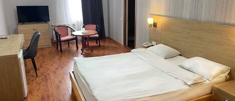 Habitación de hotel con cama, escritorio, dos sillas, televisor y puerta.