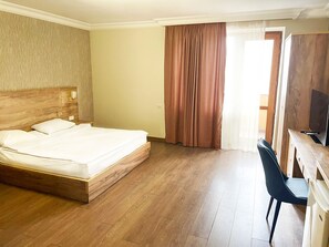 A hotel room with a wooden bed, a desk with a chair, and a television. - Primer Hotel (Yerevan)