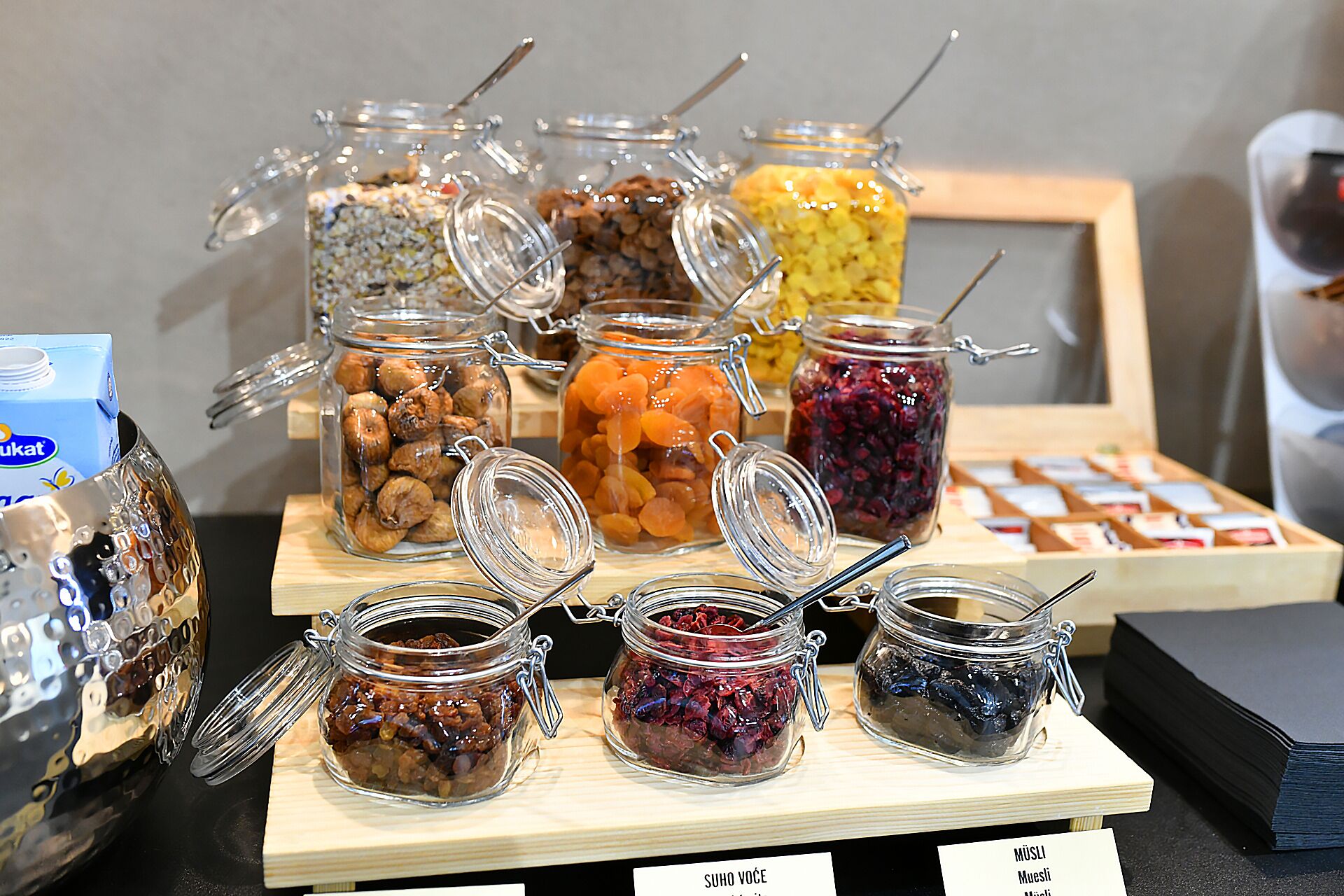 Une exposition de divers produits alimentaires présentés dans des bocaux en verre fermés par des attaches métalliques, notamment des noix, des fruits secs et des confitures.
