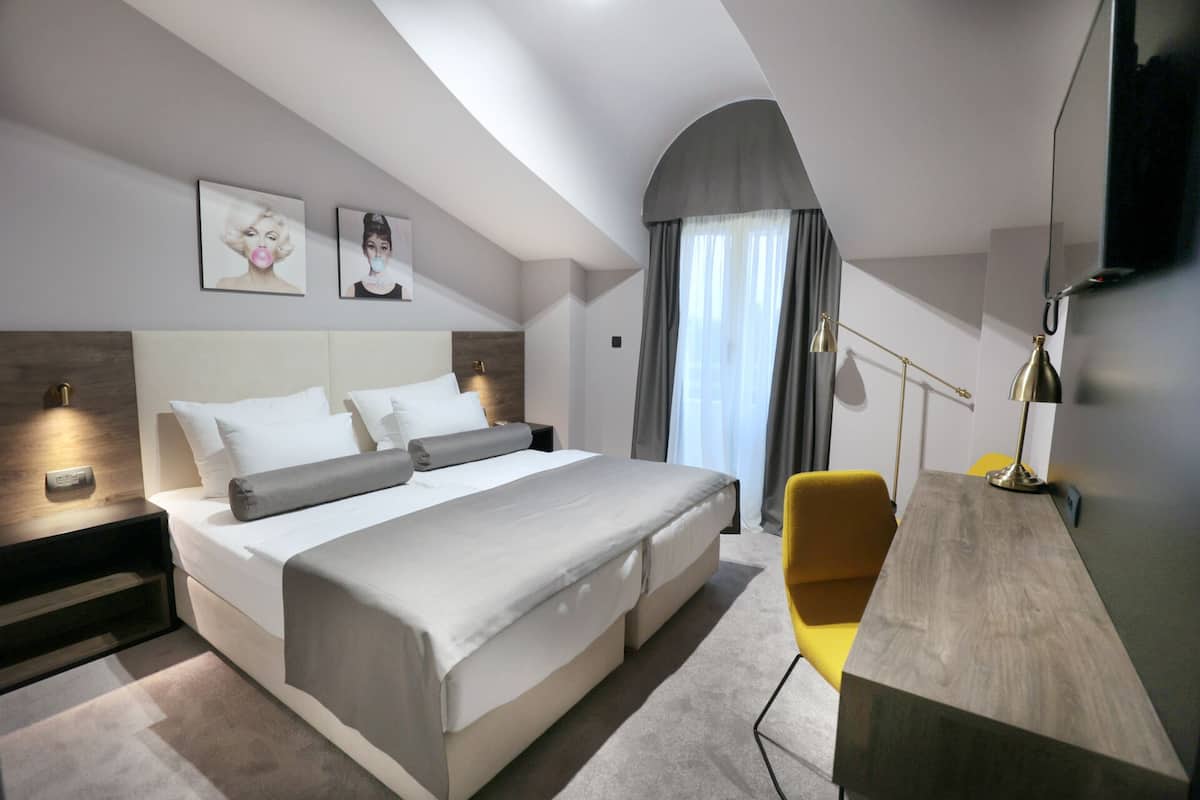 A modern hotel room with a large bed, a desk, a chair, and artwork on the wall.