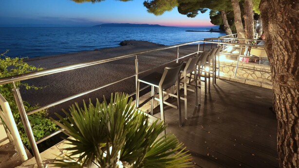 A seaside walkway with metal railings, wooden steps, and a view of the ocean at sunset. - Hotel Milenij (Makarska)
