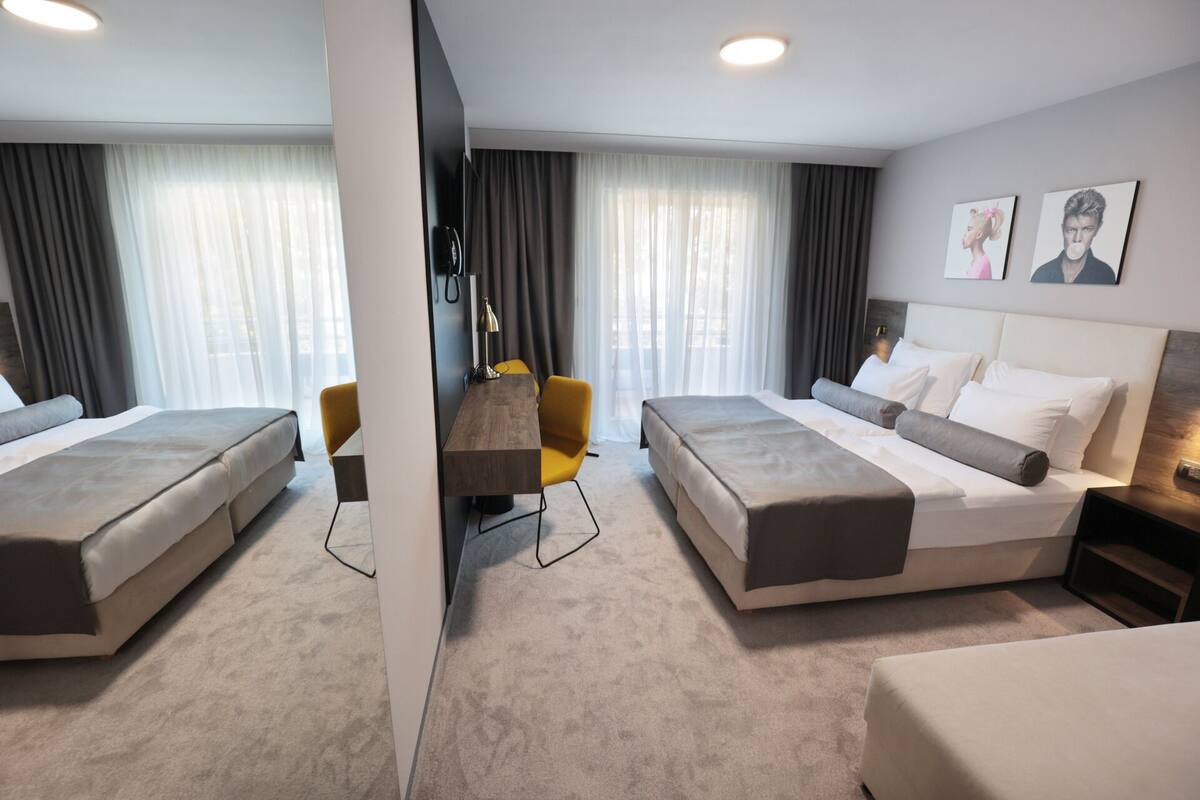 A hotel room with two beds, a desk, a chair, and a TV.