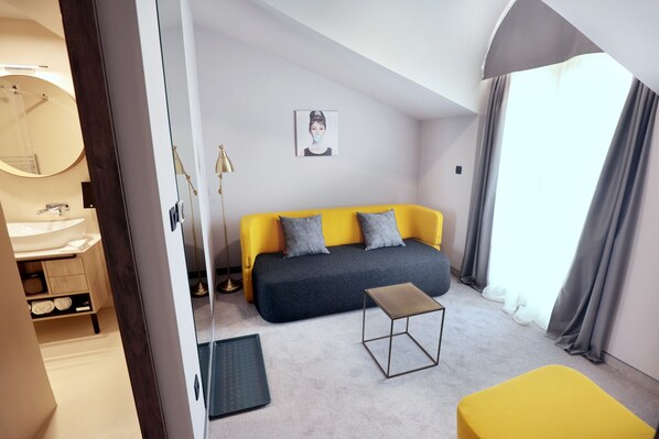 Un dormitorio moderno con un sofá amarillo, una mesita, un espejo y una lámpara de noche.