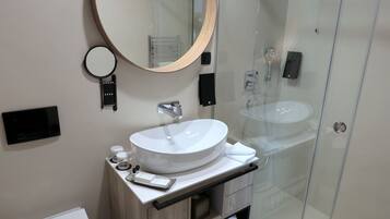 Une salle de bain moderne avec un miroir rond, un lavabo blanc et une douche à parois de verre.