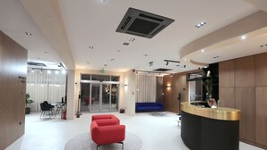 A modern reception area with a curved black reception desk, a red sofa, and a blue couch. - Hotel Milenij (Makarska)