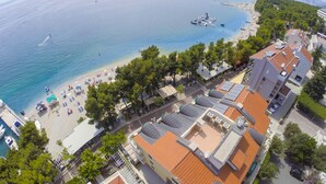 A coastal town with a beach, boats, and buildings with red roofs. - Hotel Milenij (Makarska)