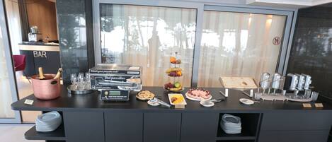 A breakfast bar with a self-service pancake station, a bar area, and a display of breakfast items including pancakes, fruits, and pastries.