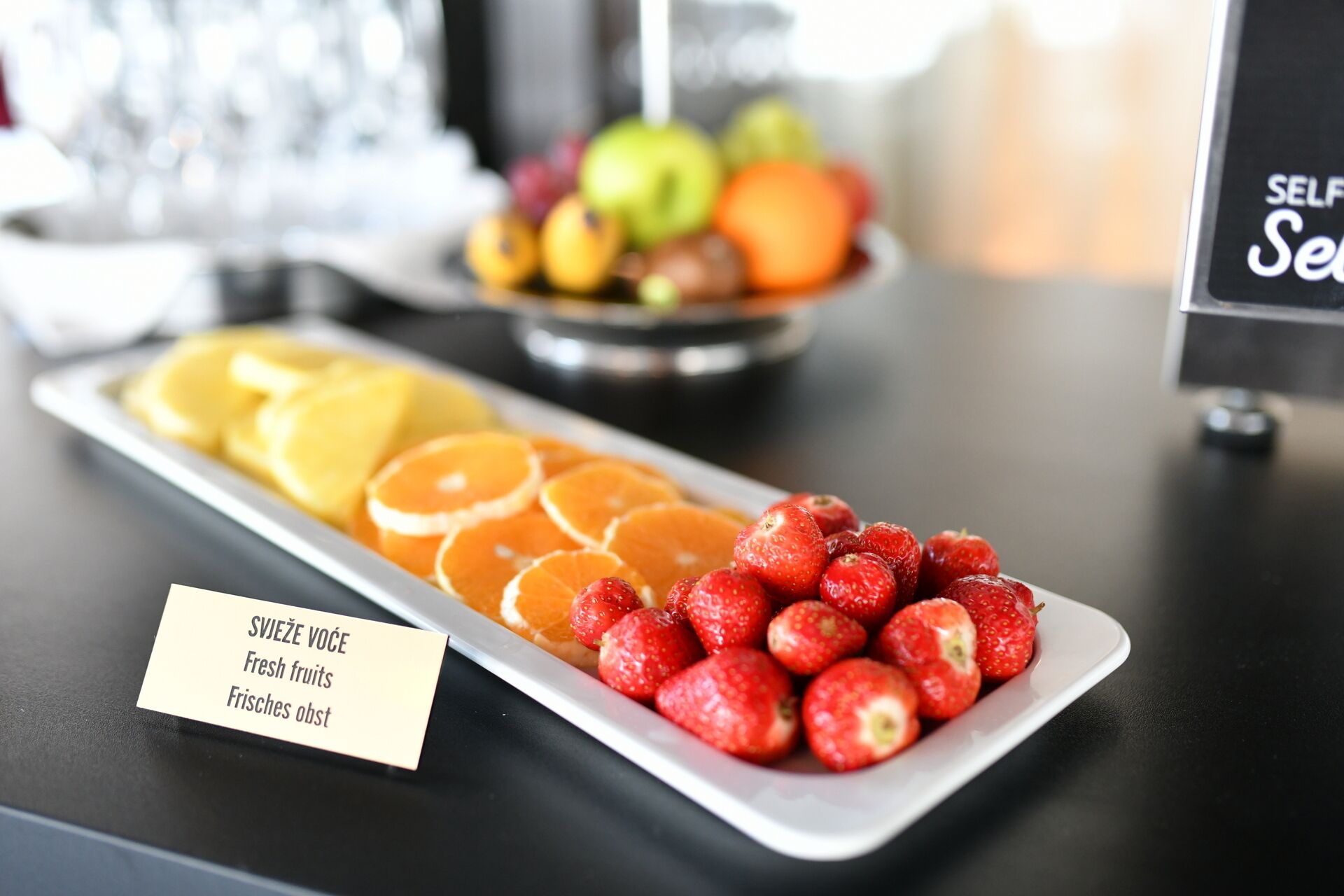 Una mesa de buffet con un cartel que indica 'Frutas frescas' en varios idiomas.