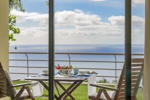 A balcony with a table set for dining, overlooking a body of water and a clear sky. - Casa do Papagaio Verde (Funchal)