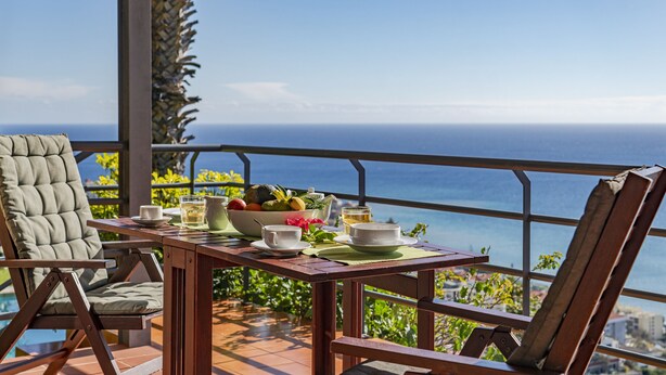 A table set with a fruit bowl, cups, and a pitcher, overlooking a scenic ocean view. - Casa do Papagaio Verde (Funchal)
