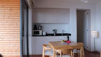 Una cucina compatta con mobili bianchi, un forno a microonde, un tostapane e un lavello. C'è un tavolo da pranzo con sedie e una piccola ciotola di frutta sopra.