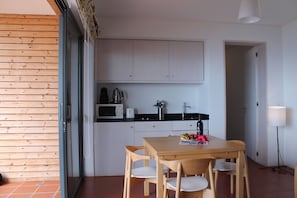 A compact kitchen with white cabinets, a microwave, a toaster, and a sink. There is a dining table with chairs and a small fruit bowl on it. - Casa do Papagaio Verde (Funchal)