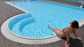 Un área de piscina con un muelle de madera y una persona tomando el sol junto a la piscina.