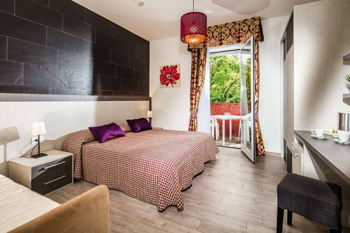 A modern hotel room with a large bed, a desk, and a view of the outdoors.