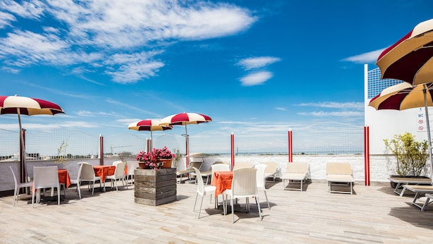 Una terraza en la azotea con asientos al aire libre, sombrillas y vistas al mar.